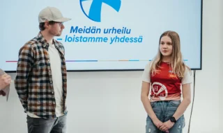 Kuvassa Lahden Hiihtoseuran mäkihypyn ja yhdistetyn valmentaja Olli Muotka ja urheilija Heta Hirvonen keskustelemassa. Taustalla Meidän urheilun logo seinällä. (Kuva: Askel Sports / Kimi Jaakkola)