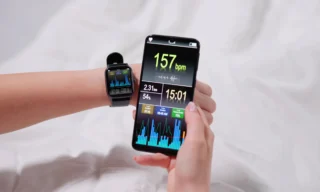 Keskellä kuvaa älypuhelin, jota pidellään kaksin käsin. Toisessa kädessä urheilukello, jossa harjoitteludataa näkyvissä. Puhelimen ruudulla jonkinlainen harjoitteluseurannan sovellus auki ja siinä numeroita ja kuvioita näkyvissä.